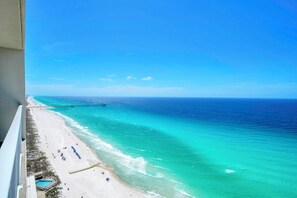 Una spiaggia con un molo che si protende nell'oceano, cieli sereni e una zona con piscina.