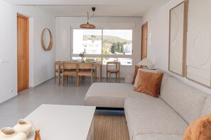Ein modernes Wohnzimmer mit Sofa, Esstisch, Stühlen, einem großen Fenster mit Blick und einer Hängelampe.