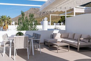 En udendørs patio med en hvid sofa, stole og et bord, med udsigt til et bjergrigt landskab.