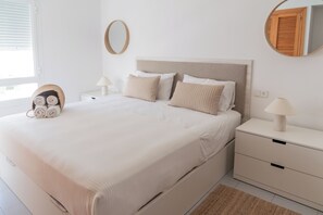 En pænt redt seng med et sengegærde, to sengeborde med lamper, et spejl og en vægmonteret lyskontakt.