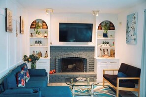 Ein Wohnzimmer mit Kamin, Flachbildfernseher, einer Couch, einem Couchtisch und Regalen mit Pflanzen.