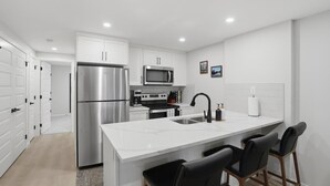 Una cocina moderna con armarios blancos, electrodomésticos de acero inoxidable y una isla central con taburetes de bar.