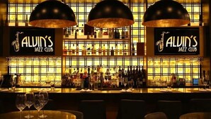 Zona de bar con letrero que dice 'ALVIN'S JAZZ CLUB', varias botellas de licor y vasos en estantes.