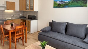 A modern kitchen with wooden cabinets, a dining table with chairs, a grey sofa, and a painting of a mountain landscape. - Prague Deluxe City Center Apartment (Hlavní město Praha)