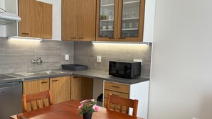 A compact kitchen with wooden cabinets, a built-in microwave, and a dining table with chairs. - Prague Deluxe City Center Apartment (Hlavní město Praha)