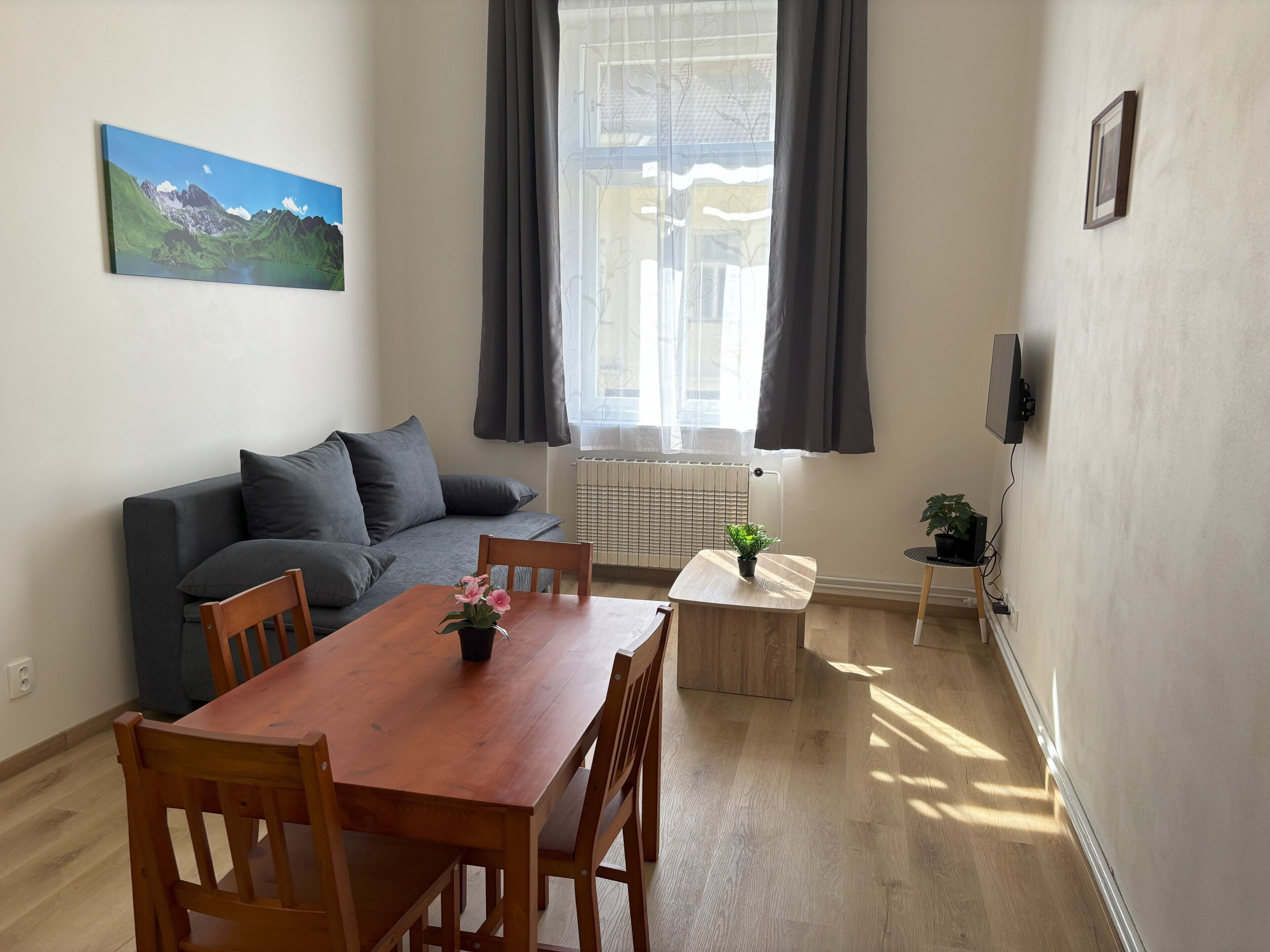 Un moderno salón con una mesa de comedor de madera, un sofá gris y un cuadro de un paisaje montañoso.