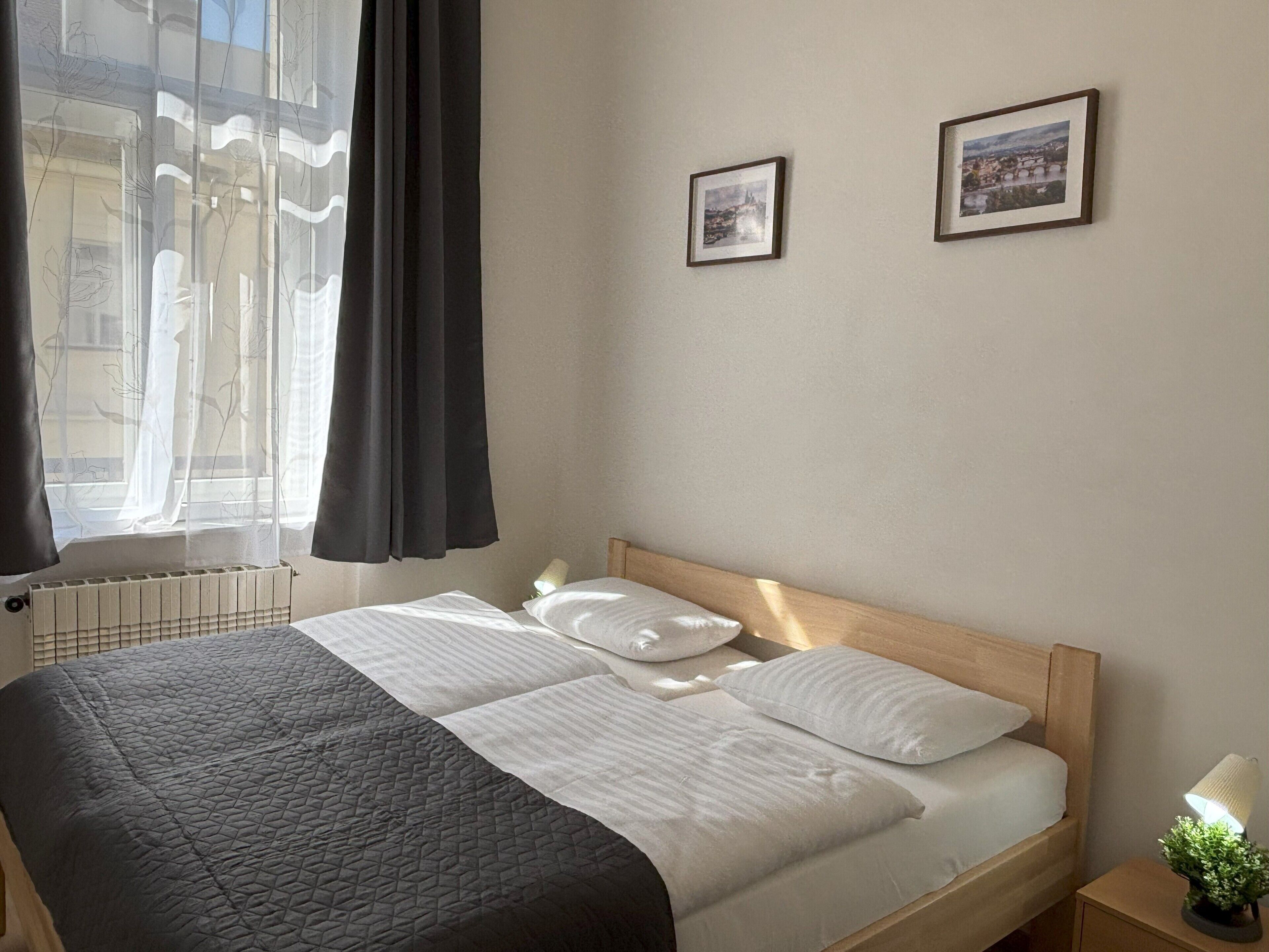 A neatly made bed with white linens, a bedside lamp, and two framed pictures on the wall.