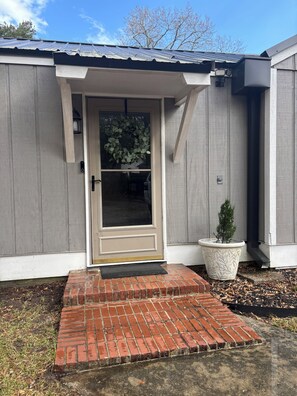 A house with a front door, a small step leading to the entrance, a potted plant, and a metal roof.