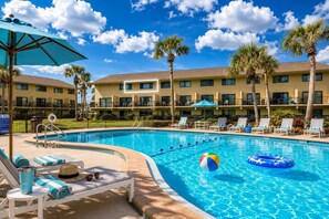 A swimming pool with lounge chairs and umbrellas, surrounded by a hotel building with multiple balconies. - Summerhouse 426: Ocean View-Beach, Pool & Tennis (St. Augustine Beach)