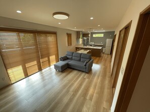 A modern living room with a grey sectional sofa, wooden flooring, and a kitchen in the background.
