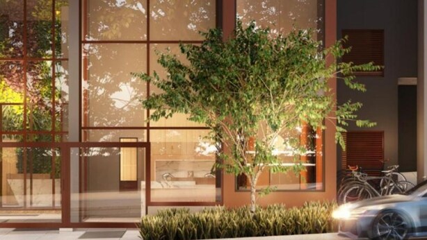 Un bâtiment moderne avec de grandes fenêtres en verre, un arbre au premier plan et une voiture garée.
