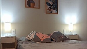 Una cama individual con dos almohadas, una mesita de noche, una lámpara y dos cuadros en la pared.