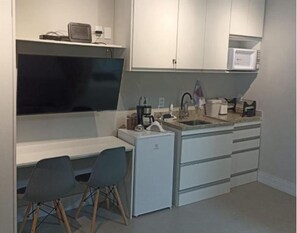 A compact kitchenette with a microwave, coffee maker, and a small refrigerator. There is a dining area with two chairs and a table. - Beautiful and recently built apartment in the Brooklin area. (São Paulo)