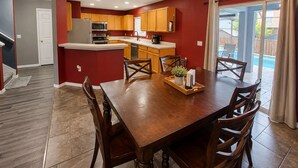 A modern kitchen with wooden cabinets, a central island, and a dining area with a wooden table and chairs. - Private Heated Pool + Spa Paradise Sleeps 9 (Seffner)