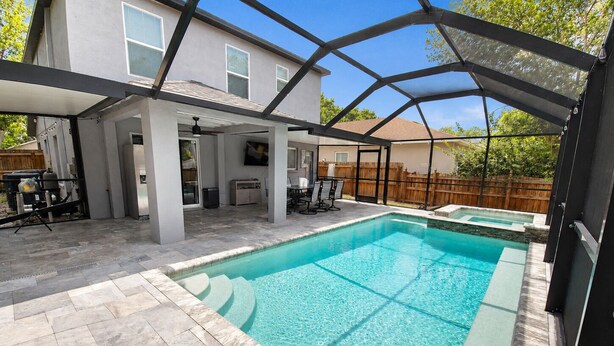 A swimming pool with a covered patio area, a small hot tub, and a house in the background. - Private Heated Pool + Spa Paradise Sleeps 9 (Seffner)