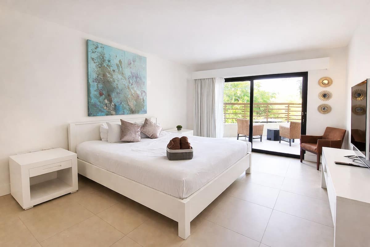 Une chambre moderne avec un grand lit, un bureau, une chaise et un balcon aménagé avec du mobilier d’extérieur.