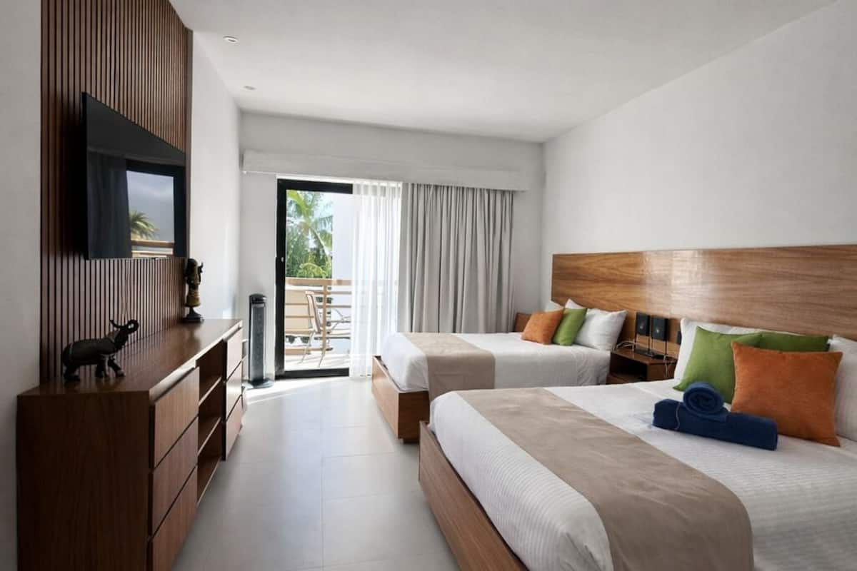 Une chambre d’hôtel moderne avec un grand lit, une télévision, une commode en bois et un balcon avec des rideaux.