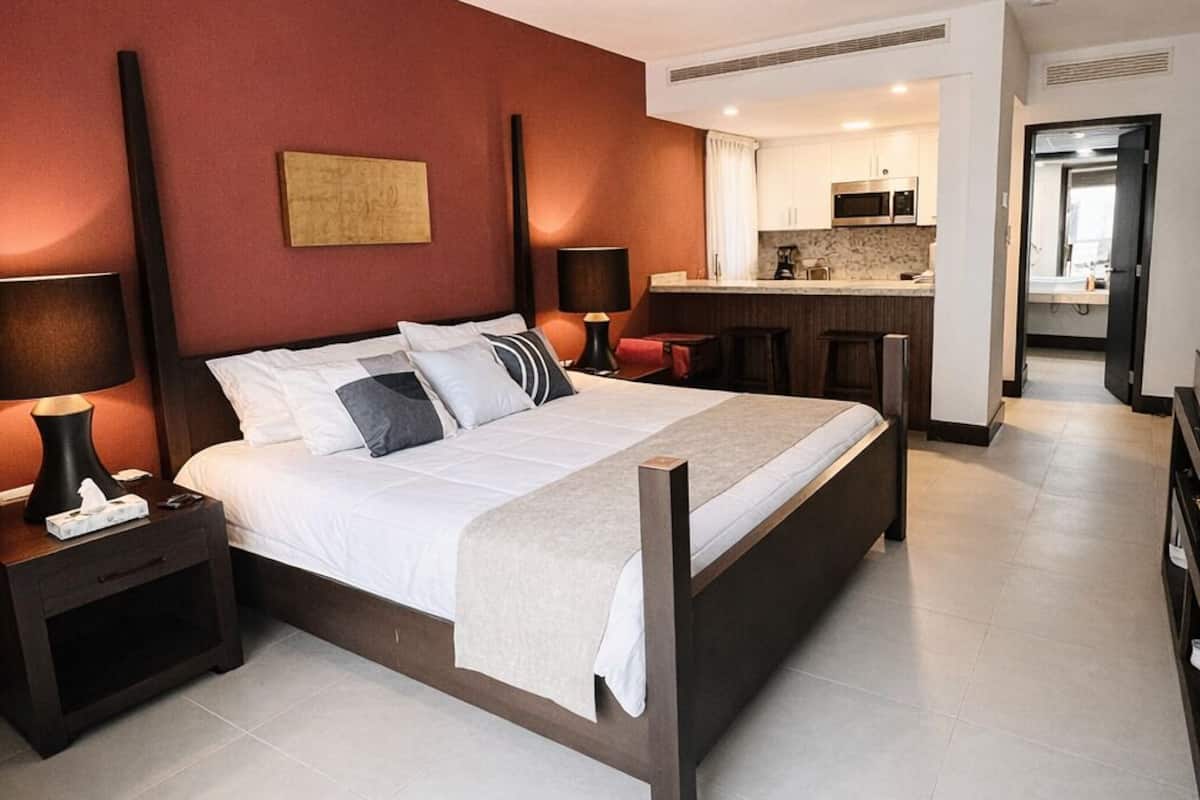 Une chambre d’hôtel moderne équipée d’un lit, de tables de chevet, d’un bureau et d’une kitchenette.
