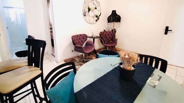 A dining area with a glass table, black chairs, and purple armchairs. - Modern Apartment in the South Zone (Uberlândia)