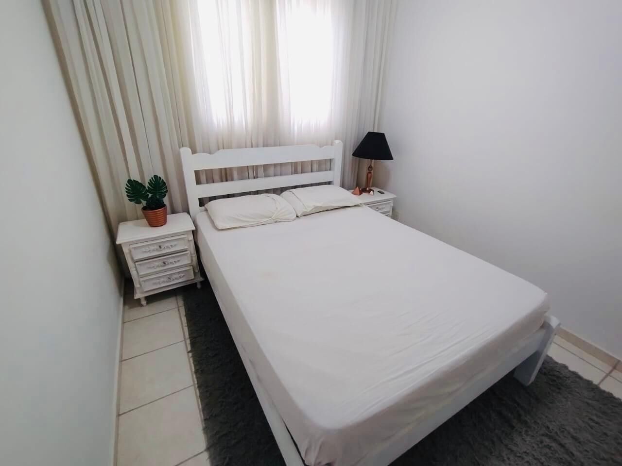 A neatly arranged bedroom with a bed, bedside table, lamp, and a small potted plant.