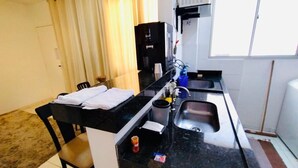 A compact kitchen with a black countertop, a coffee machine, a sink, and a window with curtains. - Modern Apartment in the South Zone (Uberlândia)