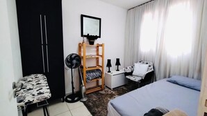 A bedroom with a bed, a desk, a chair, a wardrobe, and a standing fan. - Modern Apartment in the South Zone (Uberlândia)