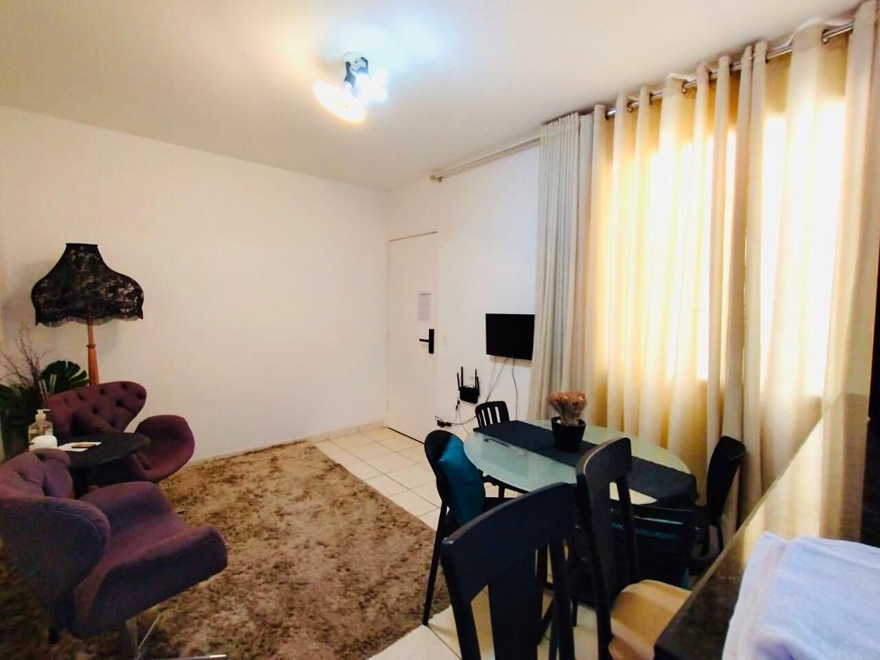 A living room with a sofa, a dining table with chairs, a TV mounted on the wall, and a window with curtains.