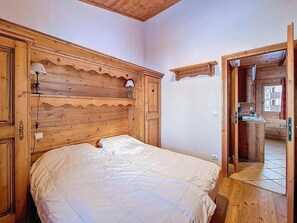 A wooden bedroom with a bed, a nightstand, a lamp, and a wooden headboard. - 3rd floor, swimming pool, terrace, tv, ski locker, 32m², Les Menuires (Les Menuires)