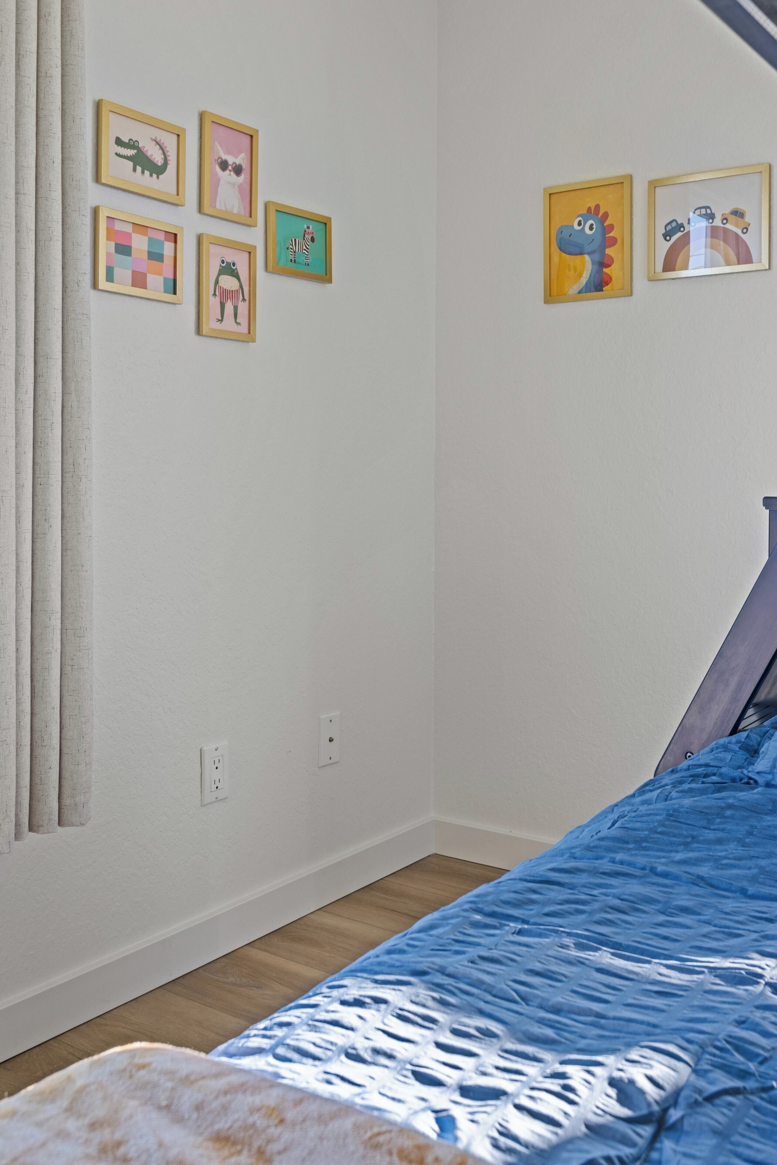 Un dormitorio con cama, ventana con cortinas e imágenes colgadas en la pared.