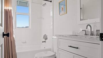 A bathroom with a bathtub, toilet, and vanity with a mirror and lights.