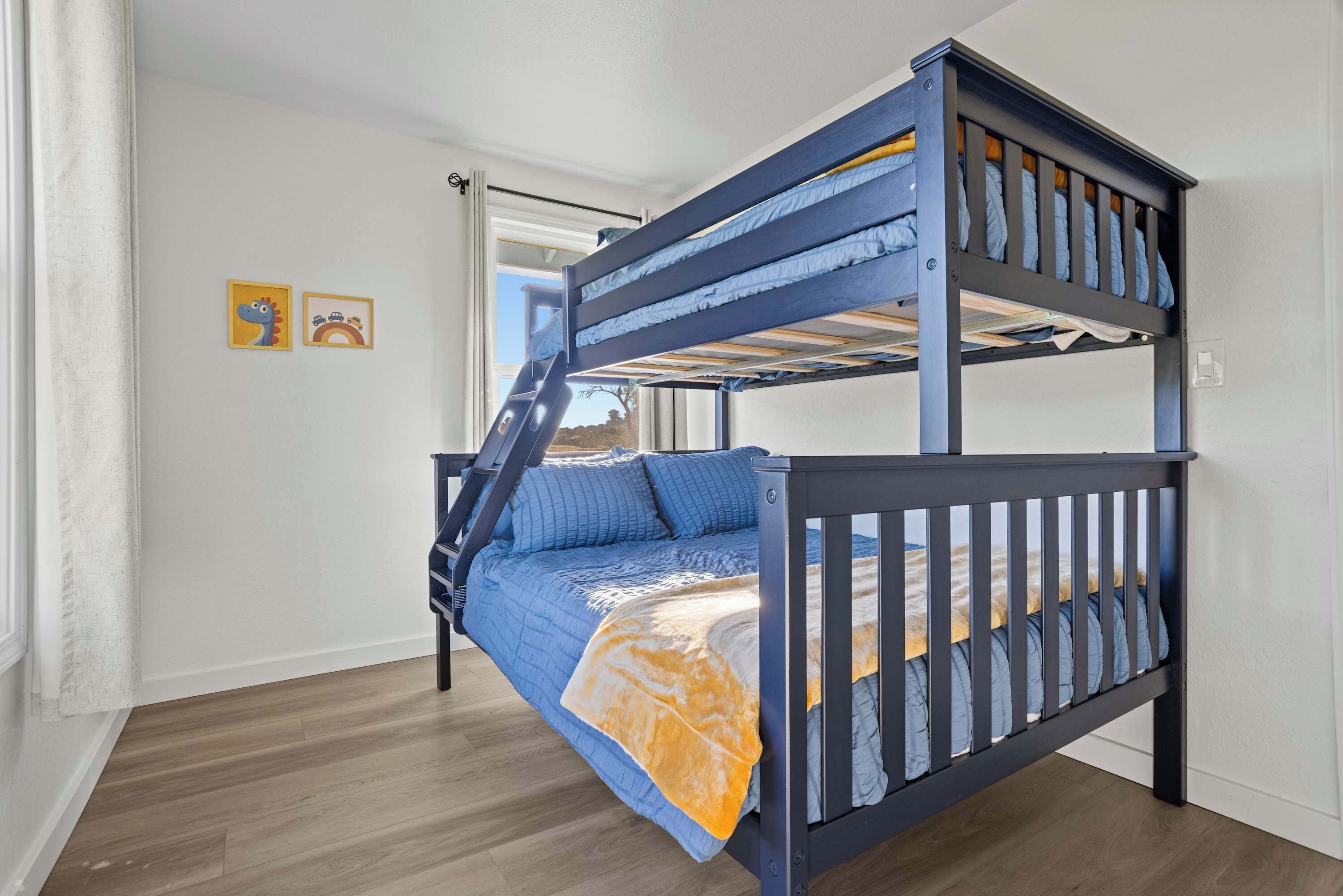 A bunk bed with a ladder, a window with a view, and two framed pictures on the wall.