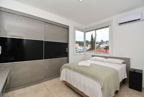 Un dormitorio con cama, ventana, armario y mesita de noche.