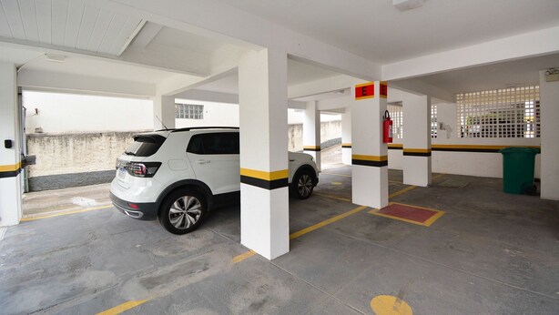A parking garage with white pillars, yellow and black stripes, and a white car parked. - Apartamento na Trindade - CEN008 (Florianópolis)
