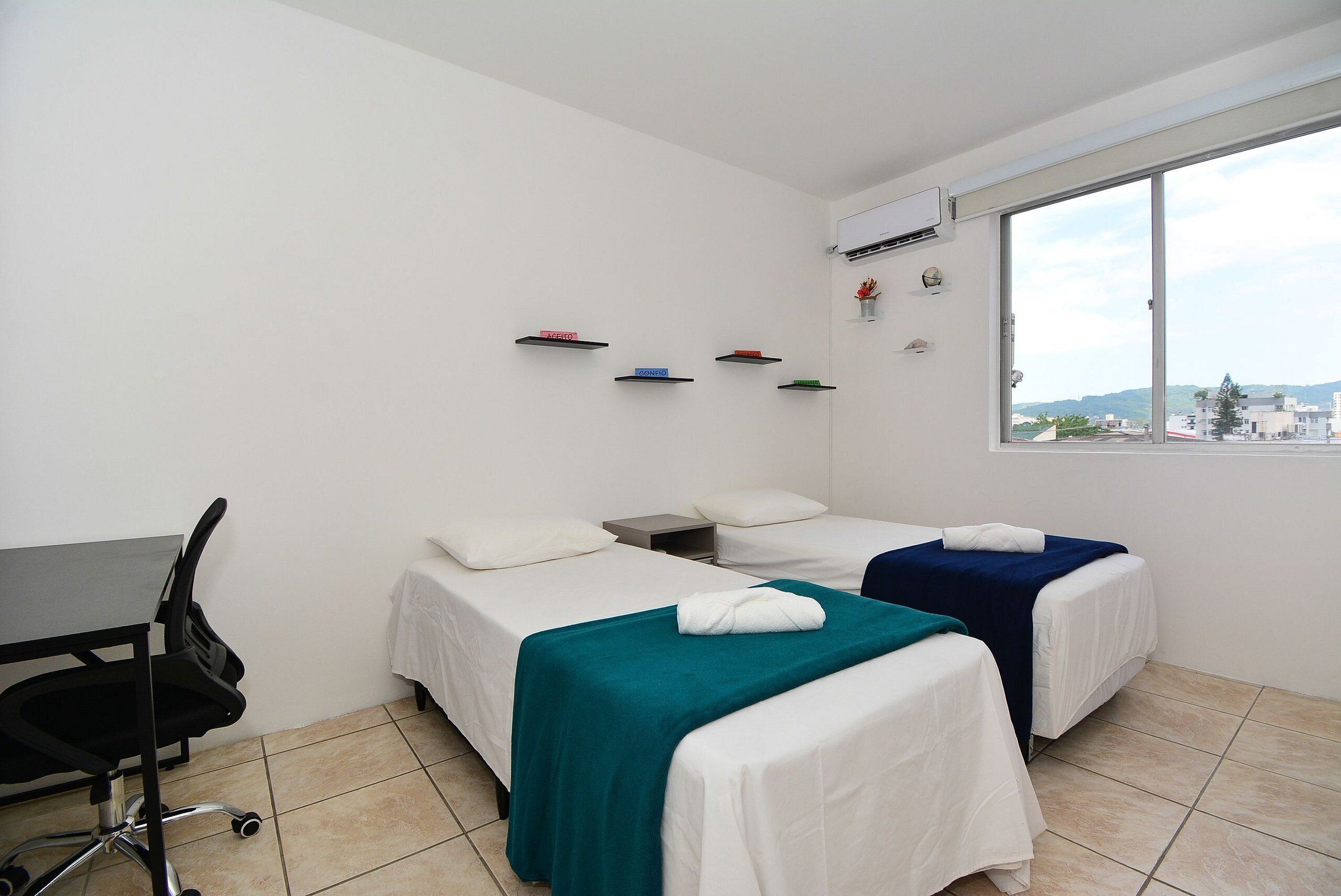 Habitación de hotel con dos camas, un escritorio, una silla y ventana con vista a la ciudad.