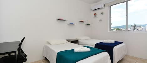 A hotel room with two beds, a desk, a chair, and a window with a city view.