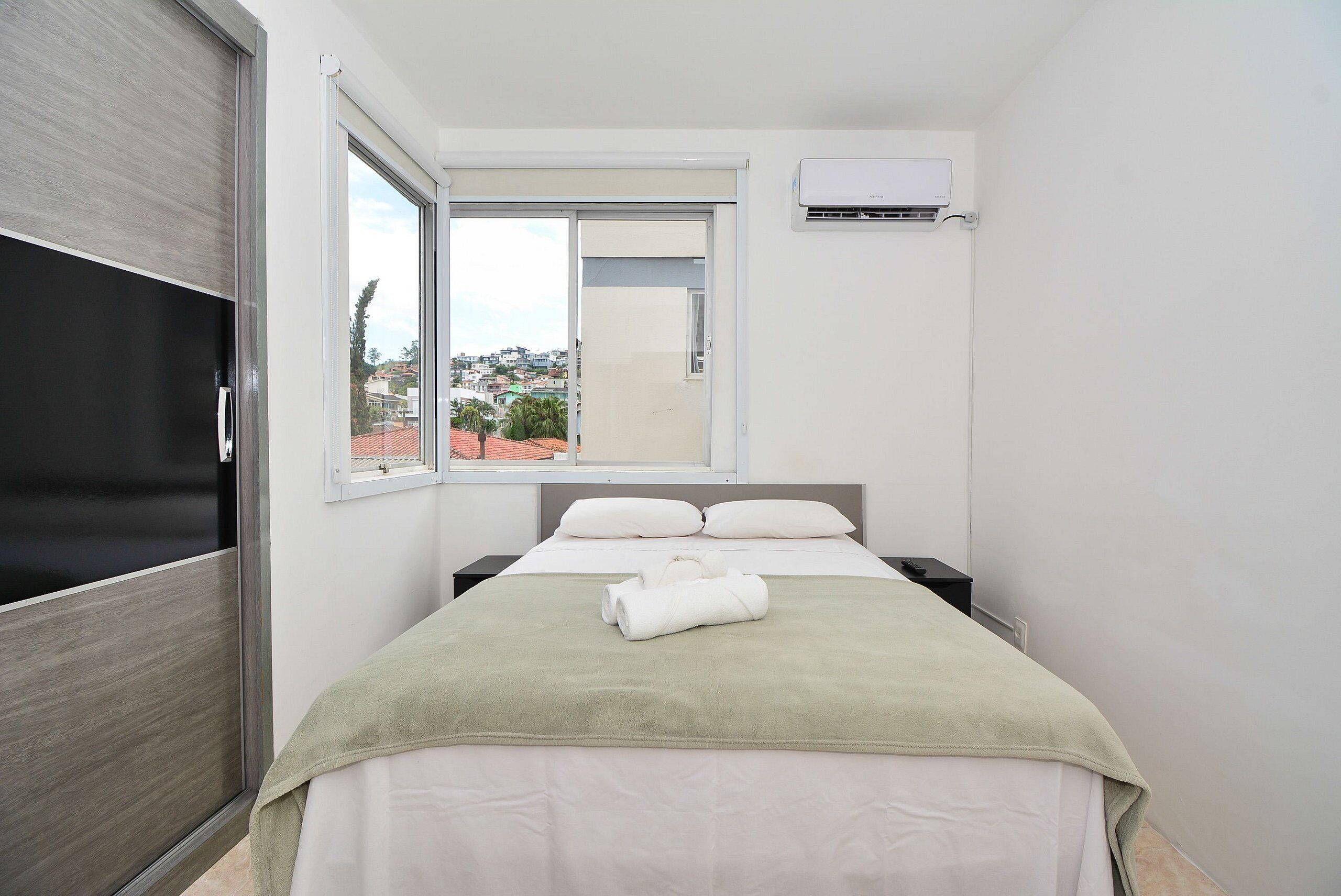 A bedroom with a bed, a window, an air conditioning unit, and a door.