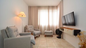A living room with a sofa, armchair, ottoman, floor lamp, TV, and a fan. - Apartamento na Trindade - CEN008 (Florianópolis)