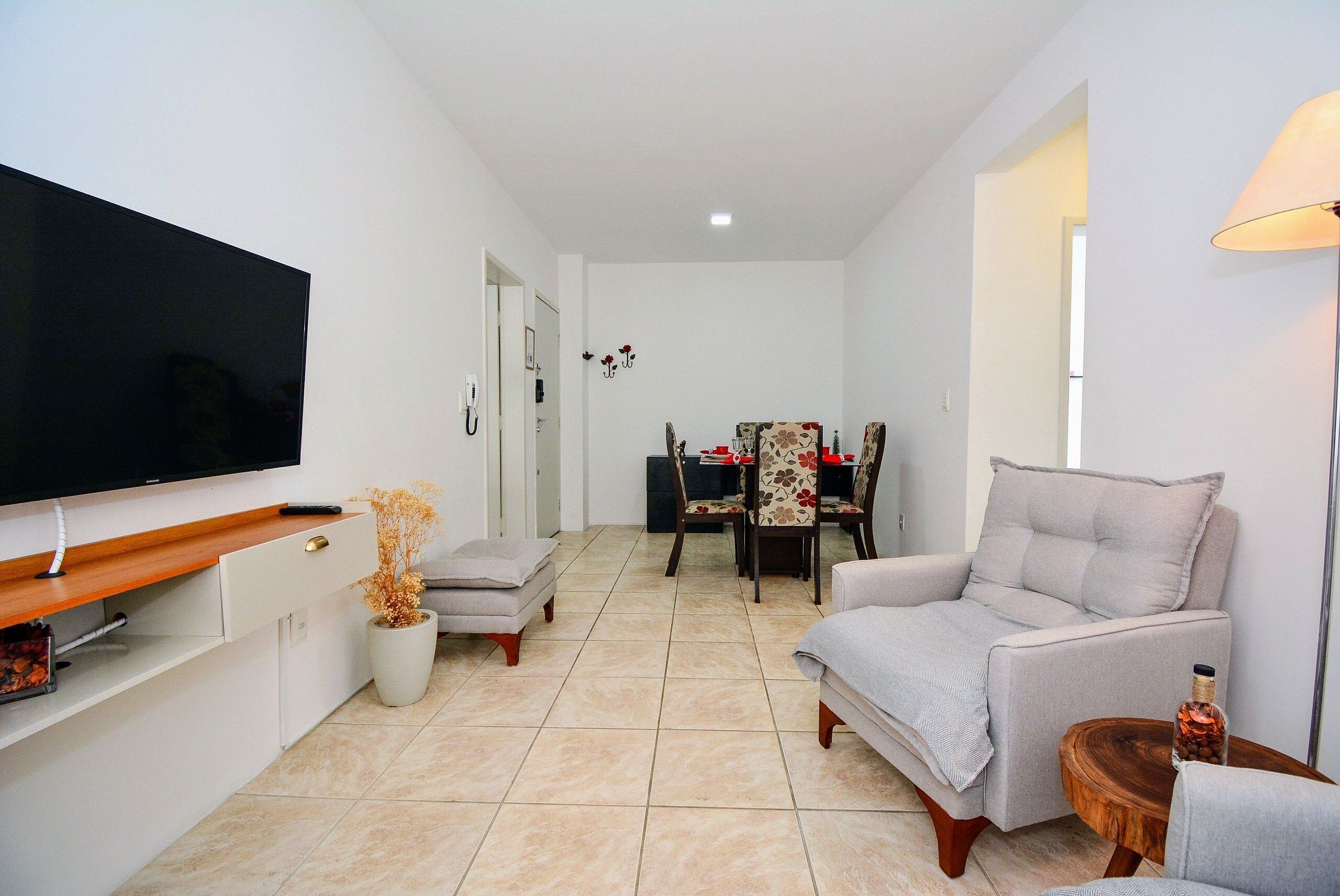Una sala de estar con televisión de pantalla plana, un sofá, una mesa de comedor con sillas y una planta en maceta.