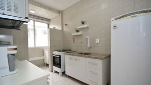 A kitchen with white cabinets, a built-in oven, a refrigerator, and a window with a view. - Apartamento na Trindade - CEN008 (Florianópolis)