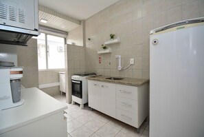 A kitchen with white cabinets, a built-in oven, a refrigerator, and a window with a view. - Apartamento na Trindade - CEN008 (Florianópolis)
