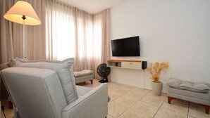 A modern living room with a sofa, a standing fan, a TV mounted on the wall, and a potted plant. - Apartamento na Trindade - CEN008 (Florianópolis)