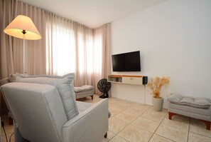 A modern living room with a sofa, a standing fan, a TV mounted on the wall, and a potted plant. - Apartamento na Trindade - CEN008 (Florianópolis)