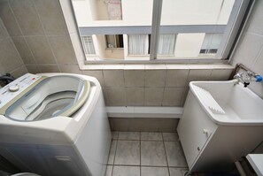 Un baño pequeño con lavadora, un lavabo y una ventana con vistas a edificios.