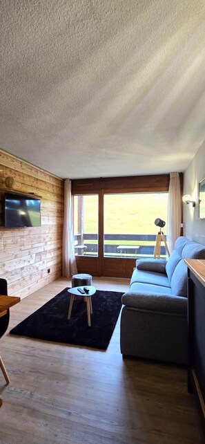 Ein modernes Wohnzimmer mit einer Holzwand, einem grauen Sofa, einem kleinen runden Tisch und einem an der Wand befestigten Fernseher.