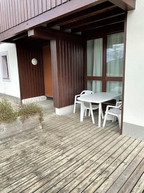A wooden deck with a table and chairs, a window with curtains, and a small plant. - 100m from ski slopes, Ground floor, terrace, tv, ski locker, 33m², Les Gets (Les Gets)