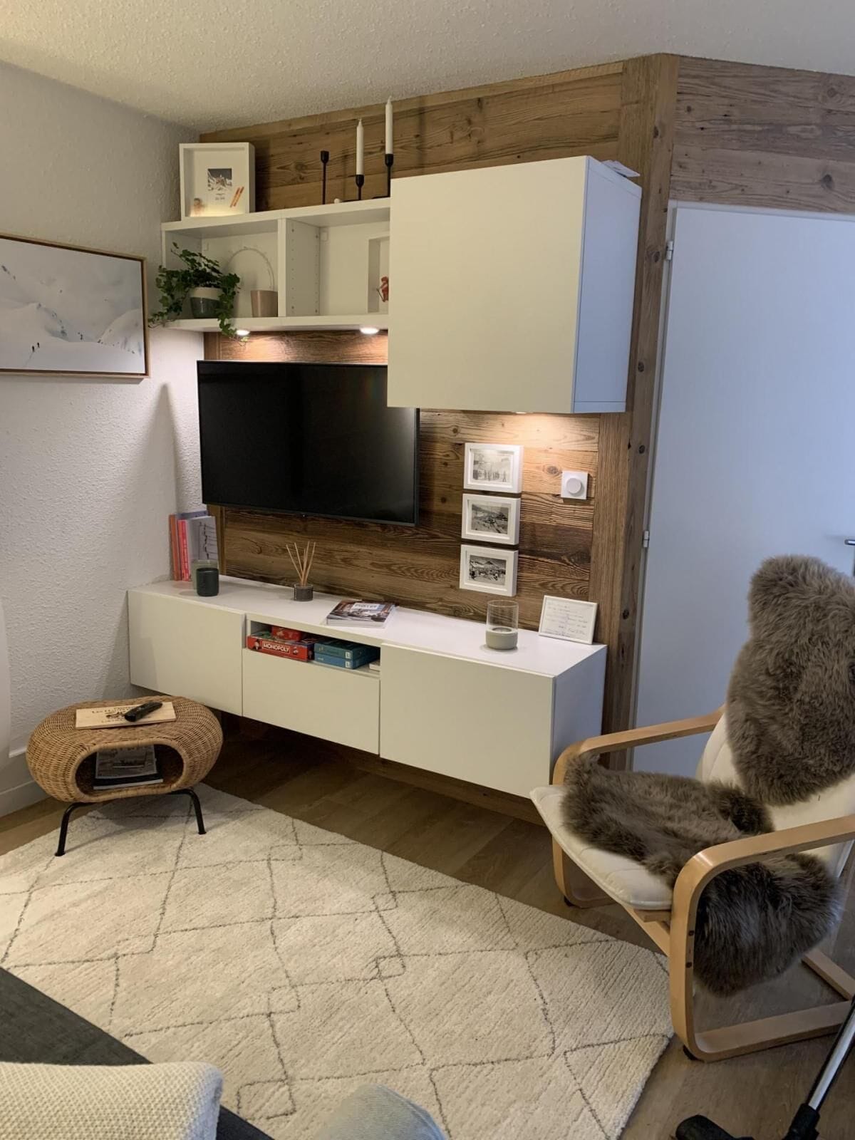 Een moderne woonkamer met een flatscreen televisie, een witte console en een comfortabele fauteuil.