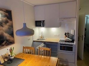 A compact kitchen with a microwave, oven, and sink. There is a dining table with chairs and a pendant light above it. - 100m from ski slopes, Ground floor, terrace, tv, ski locker, 33m², Les Gets (Les Gets)