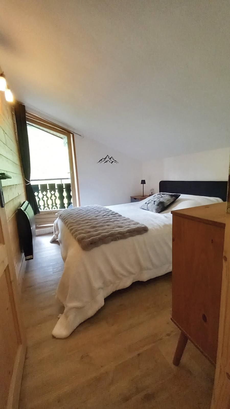 A bedroom with a bed, a nightstand, a dresser, and a window with a view of a balcony.