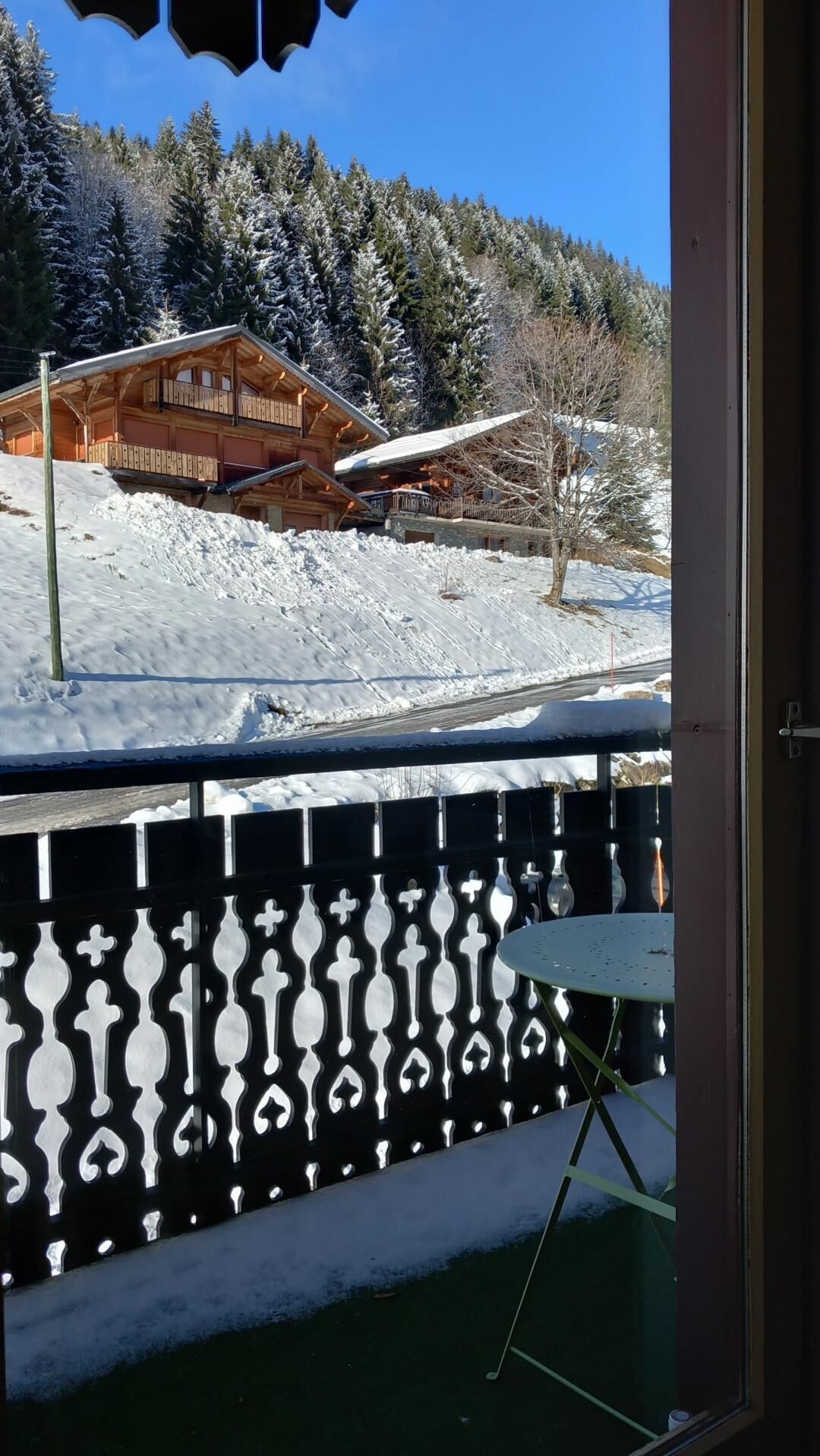 A wooden cabin with a balcony, surrounded by snow-covered trees and a clear sky.