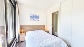 Ein Hotelzimmer mit einem Bett, Nachttischlampen, einem Fenster mit Vorhängen, einer Tür und einem Wandbild.